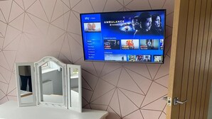 Ein Schlafzimmer mit an der Wand montiertem Fernseher, der einen Film zeigt, einem Schminktisch mit Spiegeln und einer Holztür.