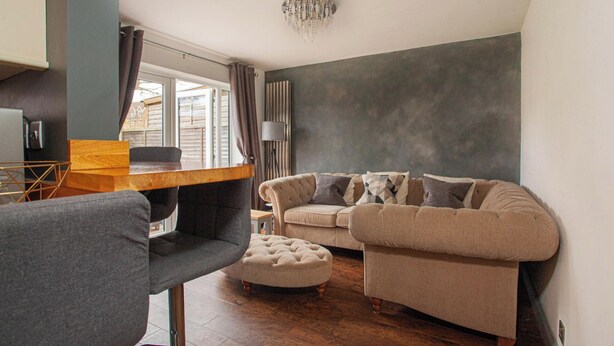Ein modernes Wohnzimmer mit einem Holzesstisch, einem grauen Sofa, einem beigen Sofa und einem gepolsterten Hocker.