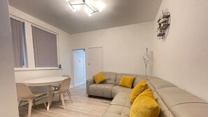 A modern living room with a grey sofa, yellow cushions, a dining table with chairs, and a ceiling light fixture. - Coast View Professional let (Whitley Bay)