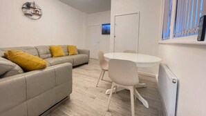 A modern living room with a grey sofa, yellow cushions, a round white table, and a ceiling light fixture. - Coast View Professional let (Whitley Bay)