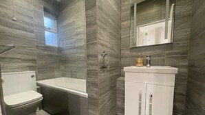 A bathroom with a toilet, a bathtub, and a sink with a mirror above it. - Coast View Professional let (Whitley Bay)