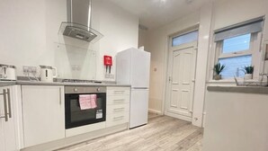 A modern kitchen with white cabinets, a built-in oven, a stainless steel range hood, and a refrigerator. - Coast View Professional let (Whitley Bay)
