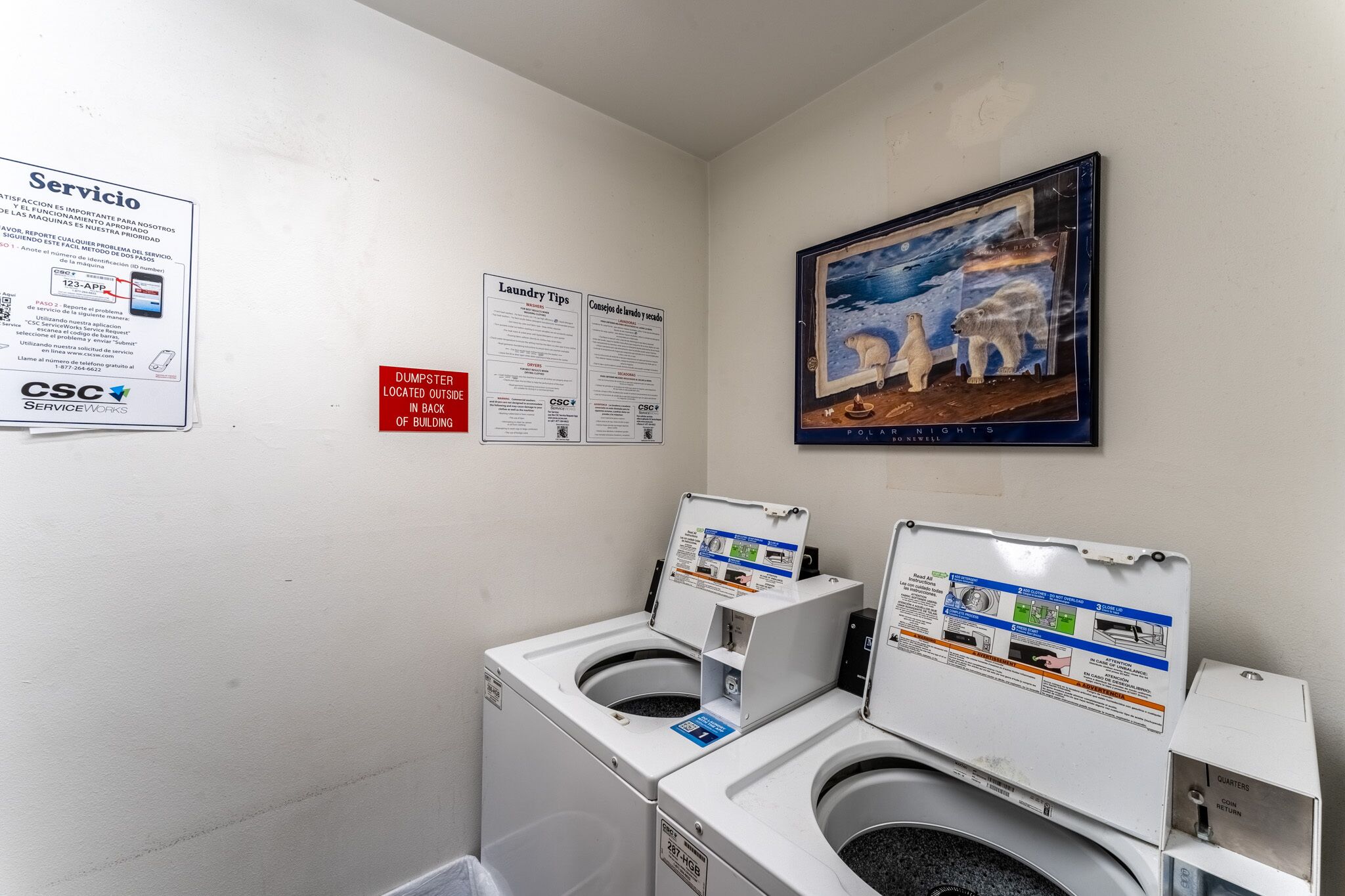 A laundry area with two washing machines, a poster of polar bears, and informational signs.