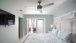 A bedroom with a bed, a ceiling fan, a TV mounted on the wall, and a view of the outside. - Tranquil Retreat by the Beach-4 bedroom 3 bath home w/private pool, parking (Key West)