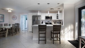 A modern kitchen with a central island, stainless steel appliances, pendant lighting, and a dining area with wooden chairs. - Tranquil Retreat by the Beach-4 bedroom 3 bath home w/private pool, parking (Key West)