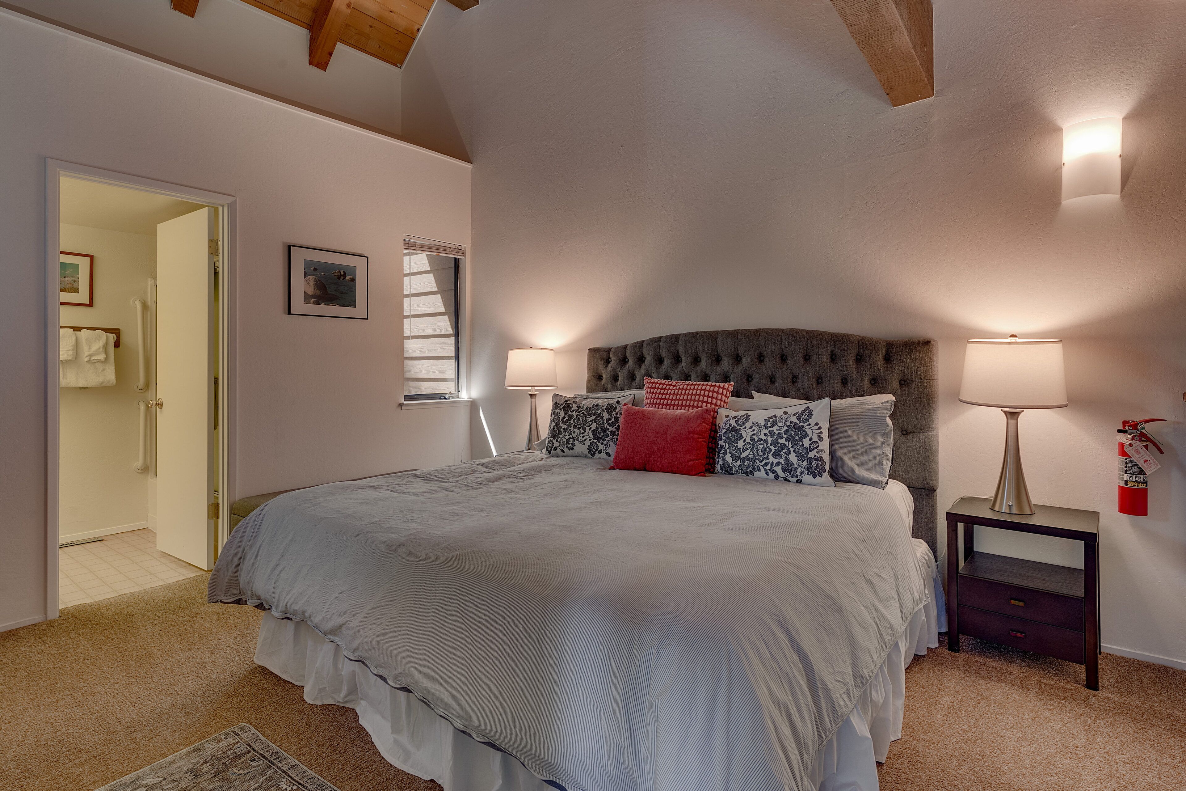 Un dormitorio con una cama grande, dos lámparas de noche, una mesita de noche y una puerta que da a otra habitación.