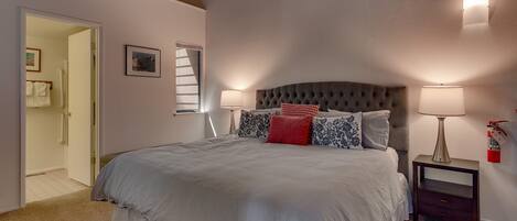 Un dormitorio con una cama grande, dos lámparas de noche, una mesita de noche y una puerta que da a otra habitación.
