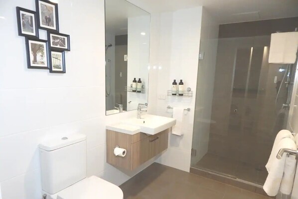 A modern bathroom with a toilet, sink, and shower. There are framed pictures on the wall and a mirror above the sink.