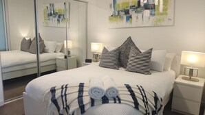 Una habitación de hotel moderna con una cama grande, un espejo, un cuadro y una mesita de noche con una lámpara.