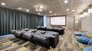 Un cine en casa con dos sillones de cuero negro reclinables, una pantalla grande y un proyector.