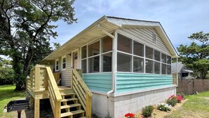 A small, single-story house with a porch and a wooden staircase leading to a deck. - Dunn In the Sun: Pet Friendly with large fenced yard. (Ocracoke)