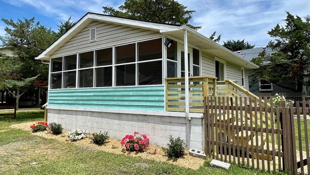 A single-story house with a front porch, a wooden fence, and a small garden with flowers. - Dunn In the Sun: Pet Friendly with large fenced yard. (Ocracoke)