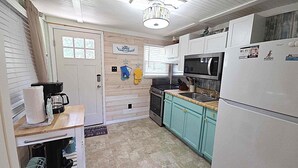 A compact kitchen with a microwave, stove, sink, and a refrigerator. - Dunn In the Sun: Pet Friendly with large fenced yard. (Ocracoke)