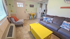 A living room with a grey sofa, yellow coffee table, and a small dining table with chairs. - Dunn In the Sun: Pet Friendly with large fenced yard. (Ocracoke)