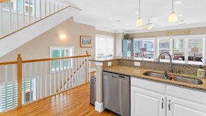 A kitchen with granite countertops, stainless steel appliances, and a view of the living area. - Lemoncello | Spacious for a Group, Elevator Access + Partial Ocean Views (Carolina Beach)
