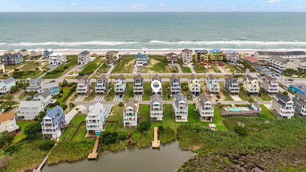Zona residencial costera con casas cerca de la playa, una masa de agua pequeña y cielo despejado.