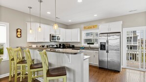Una cocina con gabinetes blancos, un refrigerador de acero inoxidable, un microondas y una barra con taburetes.