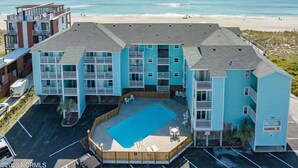 A beachfront hotel with a pool, multiple balconies, and a beach view. - Sands V 2B | Ocean Views + Near Area Fun in Carolina Beach (Carolina Beach)