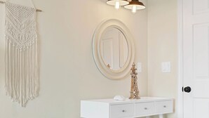 A white vanity with a round mirror, a macrame wall hanging, and a potted plant. - Sands V 2B | Ocean Views + Near Area Fun in Carolina Beach (Carolina Beach)