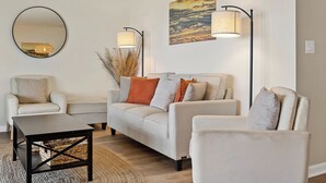 Un salon comprenant un ensemble de canapés, une table basse, un lampadaire et un miroir fixé au mur.