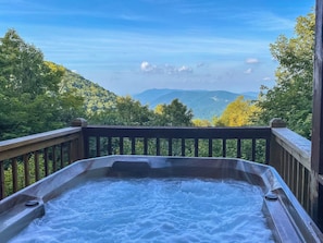 Ein Whirlpool auf einer Holzdiele mit Blick auf Berge und Bäume.