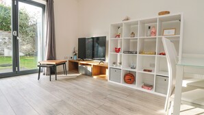 A modern living room with a wooden desk, a flat-screen TV, and a white shelving unit. - 1 Queensway Gardens (Hayle)