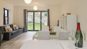 A modern living room with a sofa, dining table, and a bottle of wine. - 1 Queensway Gardens (Hayle)