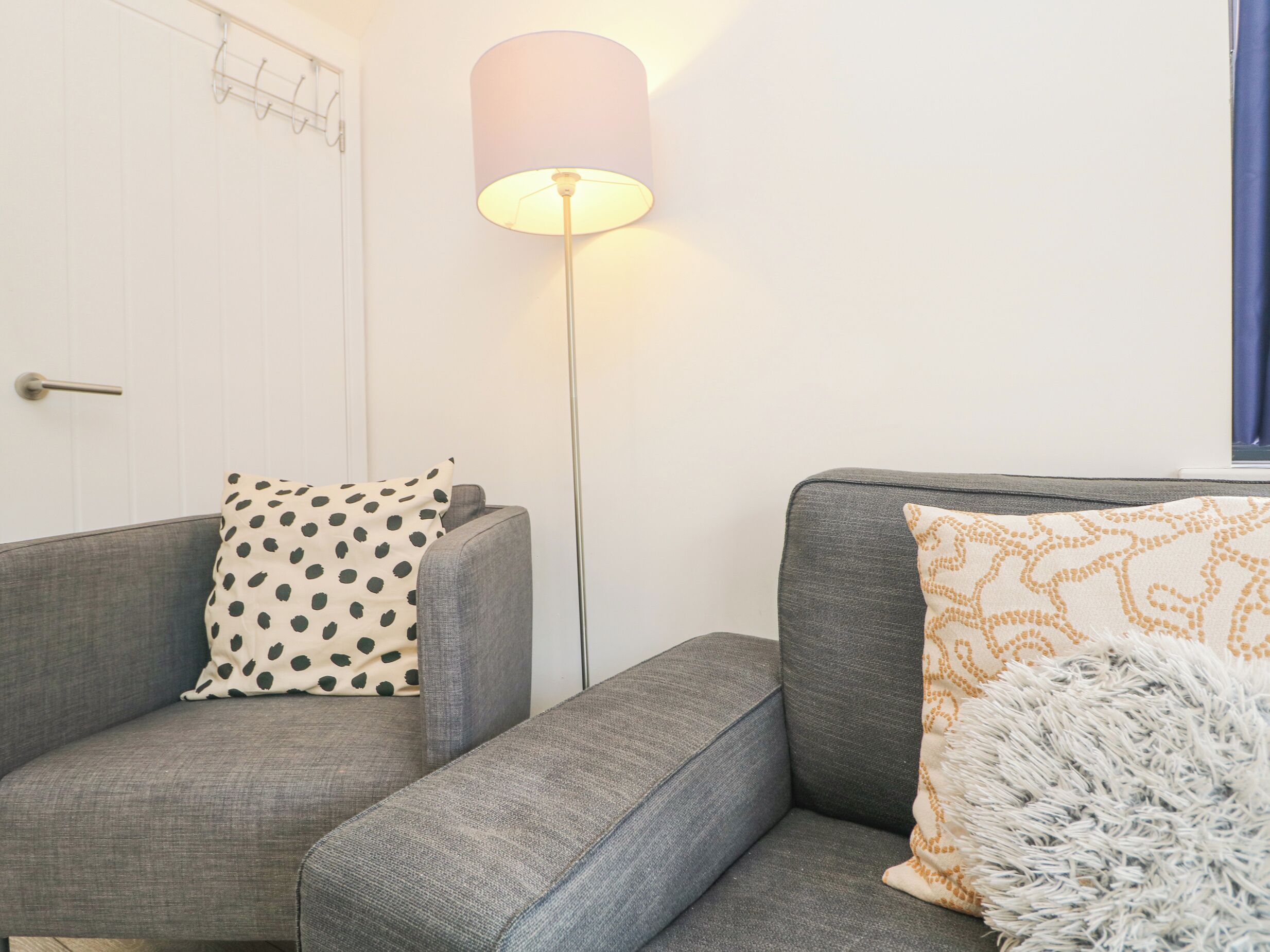 Una sala de estar moderna con un sofá gris, un cojín estampado, una manta mullida y una lámpara de pie.