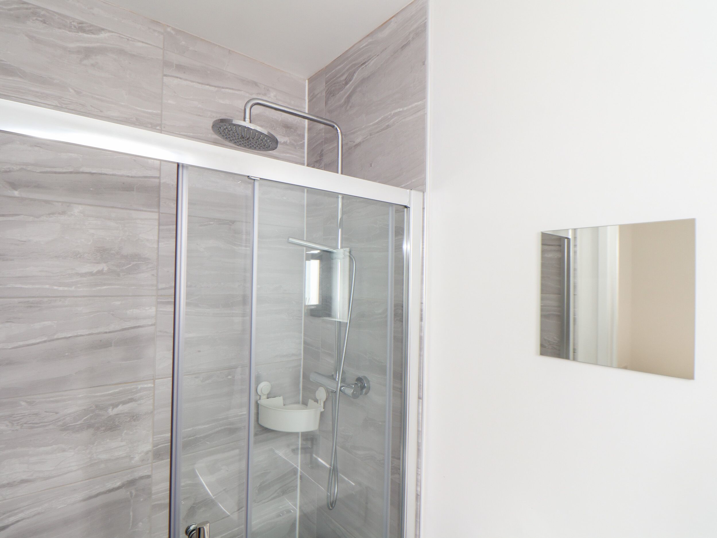 A modern shower with a glass enclosure, a handheld showerhead, and a wall-mounted control panel.