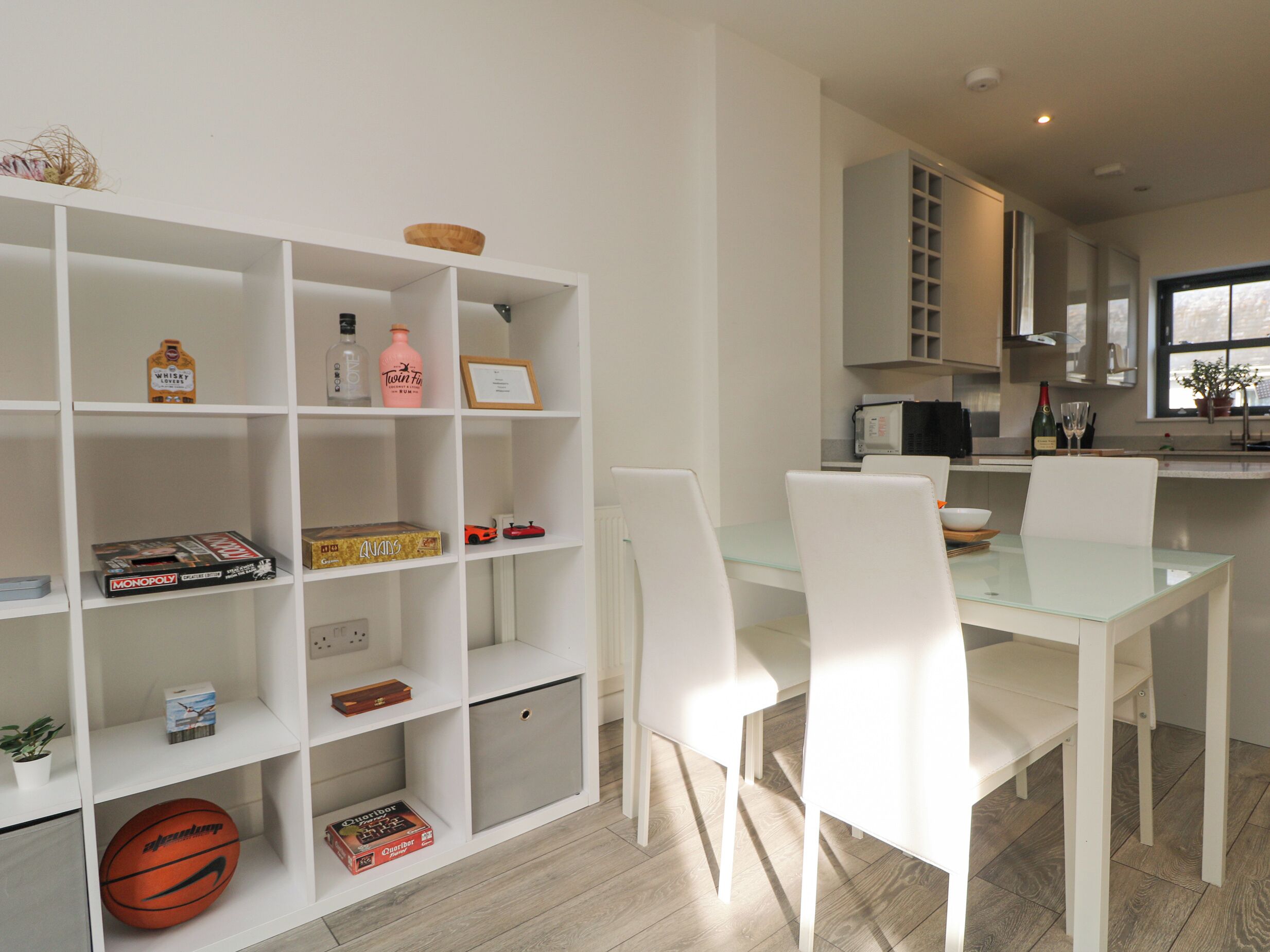 Una cocina moderna con armarios blancos, una mesa de comedor de vidrio y sillas blancas.