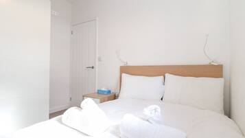A neatly made bed with white linens and two rolled towels, a wooden headboard, and a bedside table with a tissue box.