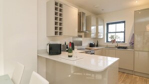A modern kitchen with a central island, built-in cabinets, stainless steel appliances, and a window providing natural light. - 1 Queensway Gardens (Hayle)