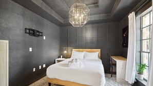 A bedroom with a wooden bed, a desk, a chair, a hanging light fixture, and a window with curtains. - Allen Abode - 4 Bedrm. Pool, Fire Pit , Charm (Allen)