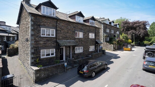 A stone-built two-story residential building with multiple windows and a sloped roof.