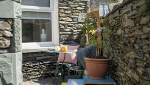 A cozy outdoor seating area with a stone wall, a window, and a potted plant.