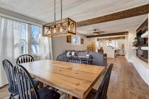 A spacious dining area with a wooden table and chairs, a hanging light fixture, and a view into the adjacent living space.