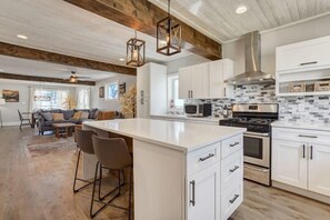 A modern kitchen with white cabinets, a central island, stainless steel appliances, and a wooden ceiling.