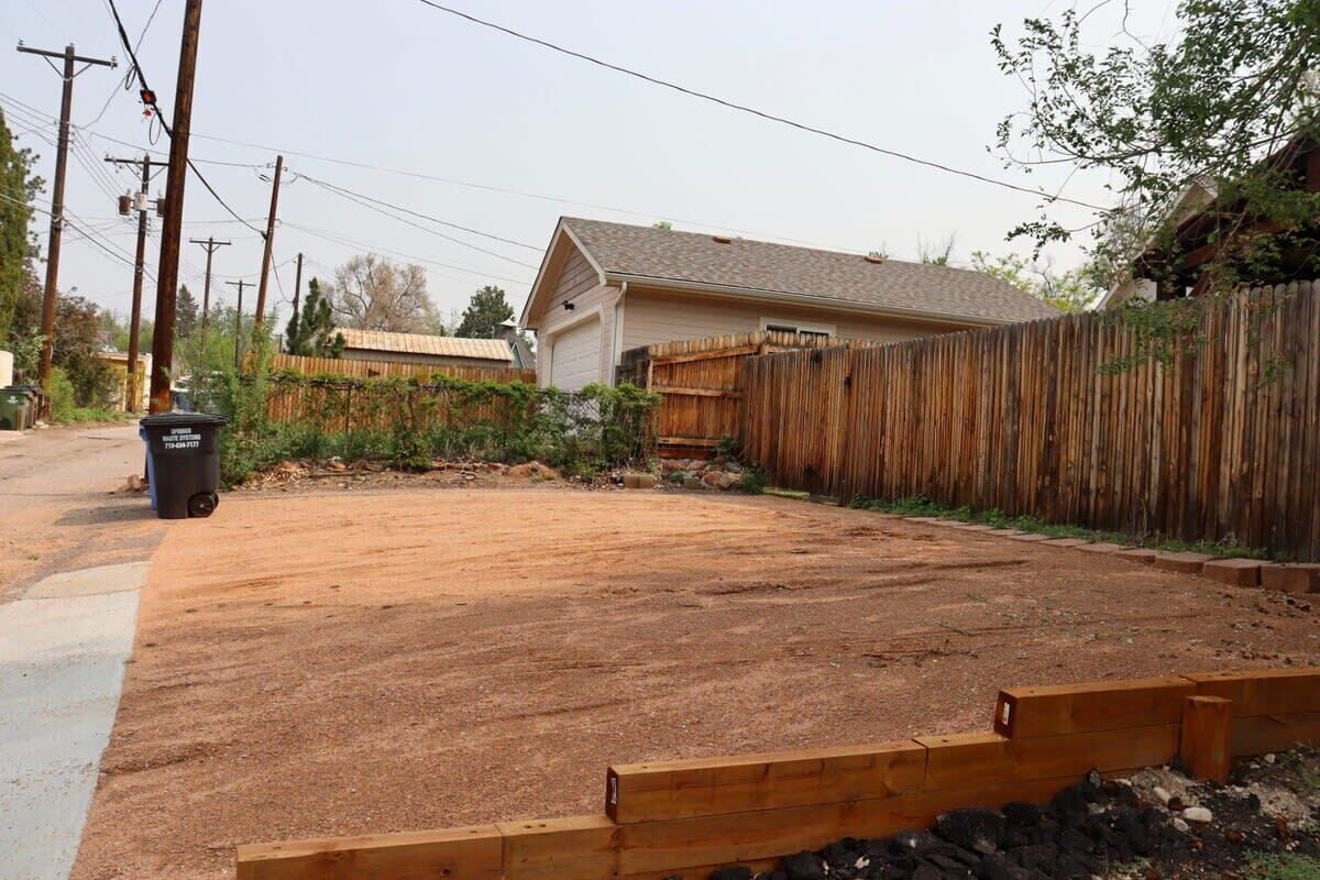 A residential backyard with a wooden fence, a dirt area, and a house in the background.