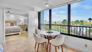 A bedroom with a bed, bedside table, lamp, and a view of the ocean through large windows. - Beachfront Condo -Gulf and Bay A205 (Siesta Key)