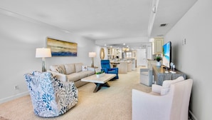 A modern living room with a sofa, armchair, and coffee table. There is a kitchen in the background with cabinets and a countertop. - Beachfront Condo -Gulf and Bay A205 (Siesta Key)