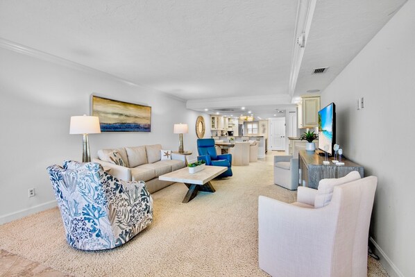 A modern living room with a sofa, armchair, and coffee table. There is a kitchen in the background with cabinets and a countertop.