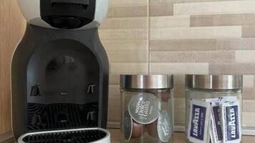 A coffee machine with a Krups brand, two glass containers with coffee pods, and a tiled backsplash.
