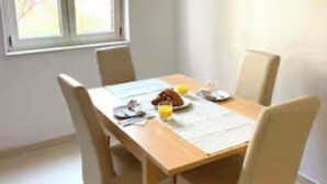 Un coin repas avec une table en bois, quatre chaises et une fenêtre donnant sur les arbres.
