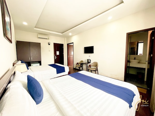 Habitación de hotel con dos camas, un escritorio, una silla, un televisor y un baño visible a través de una puerta abierta.