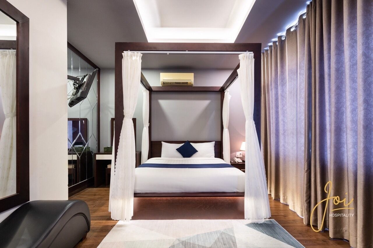 Una habitación de hotel moderna con cama con dosel, una mesita de noche y un amplio ventanal con cortinas.