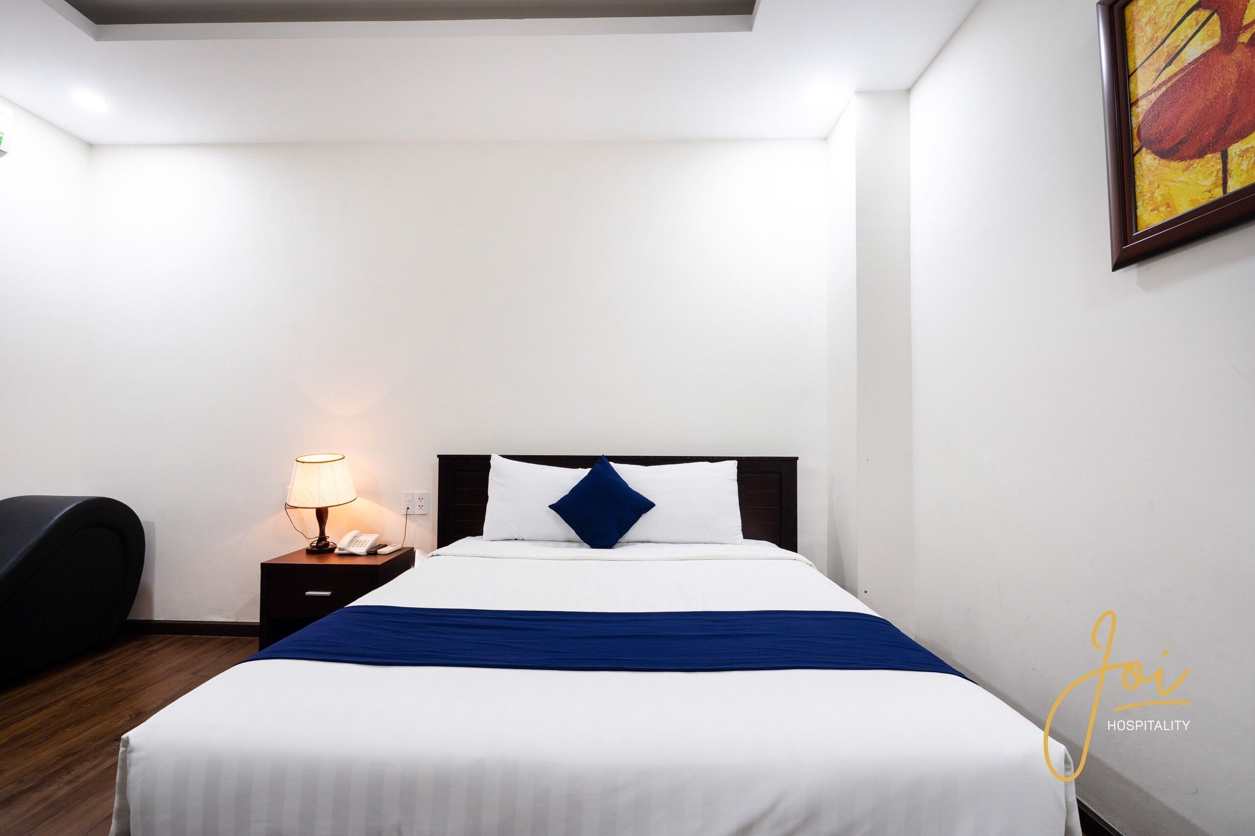 Une chambre d’hôtel avec un lit, une table de chevet avec une lampe et un tableau au mur.