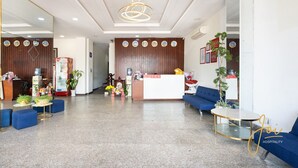 Een moderne hotellobby met een receptiebalie, blauwe banken, een koffieapparaat en een decoratieve plant.