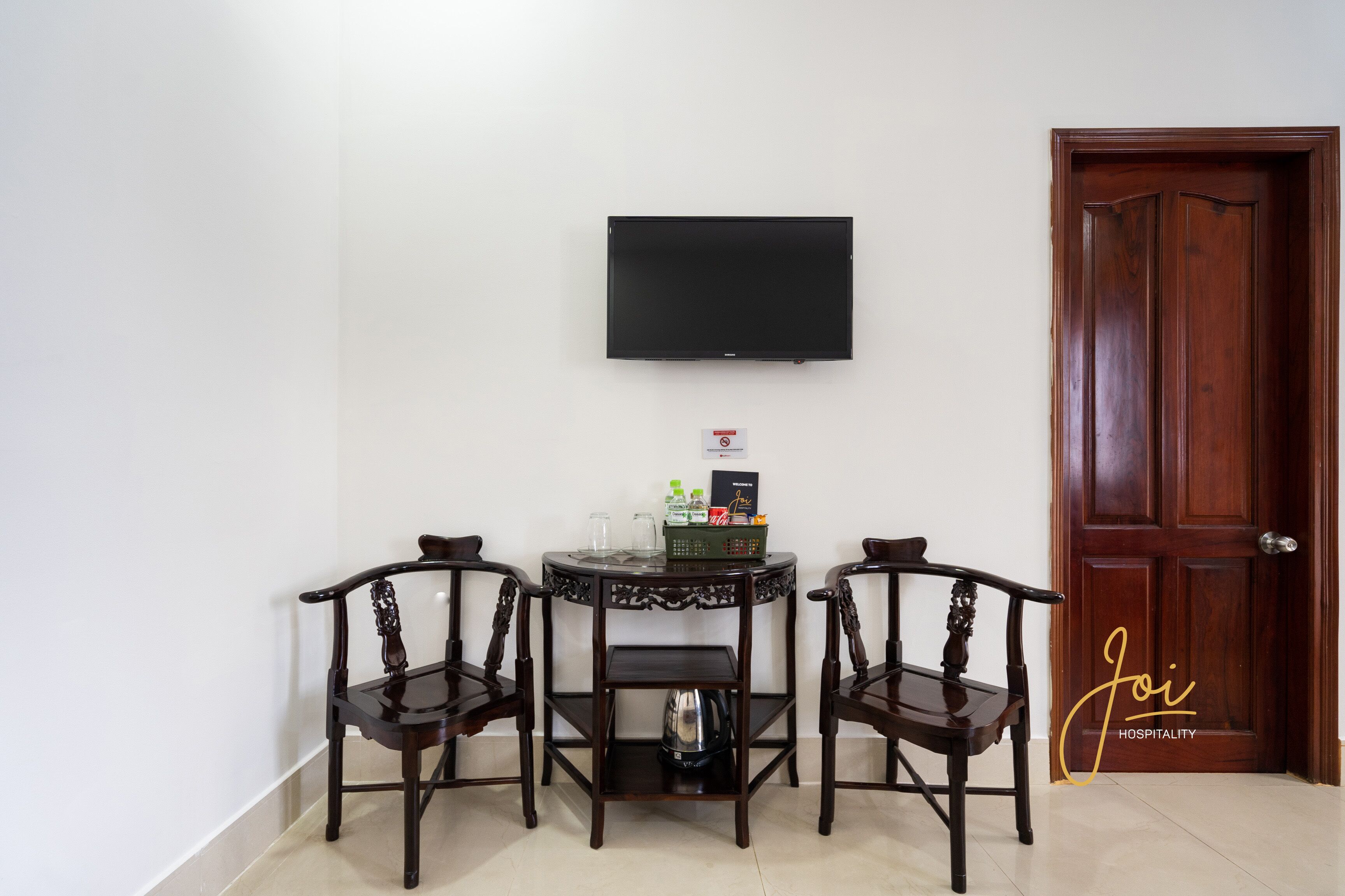 A room with a TV mounted on the wall, two wooden chairs, a small table with a basket, and a door.