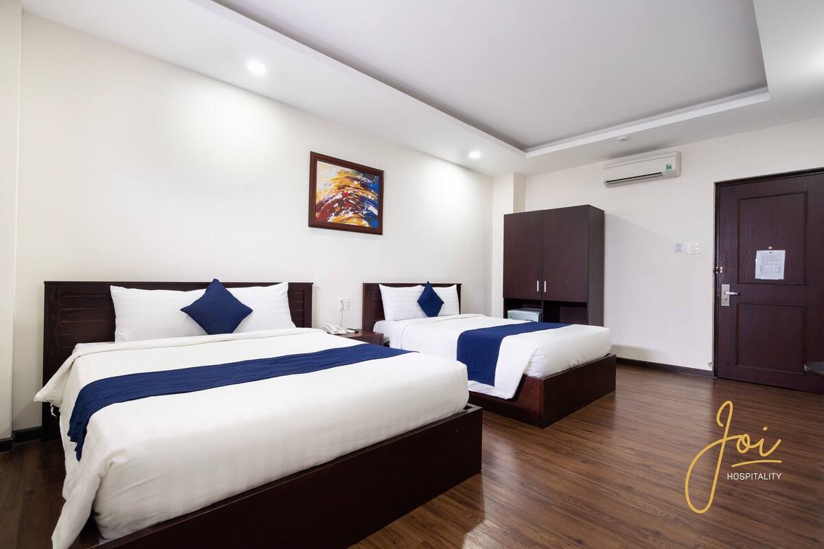 Habitació d'hotel amb dos llits, un quadre a la paret, un aparell d'aire condicionat i una porta.