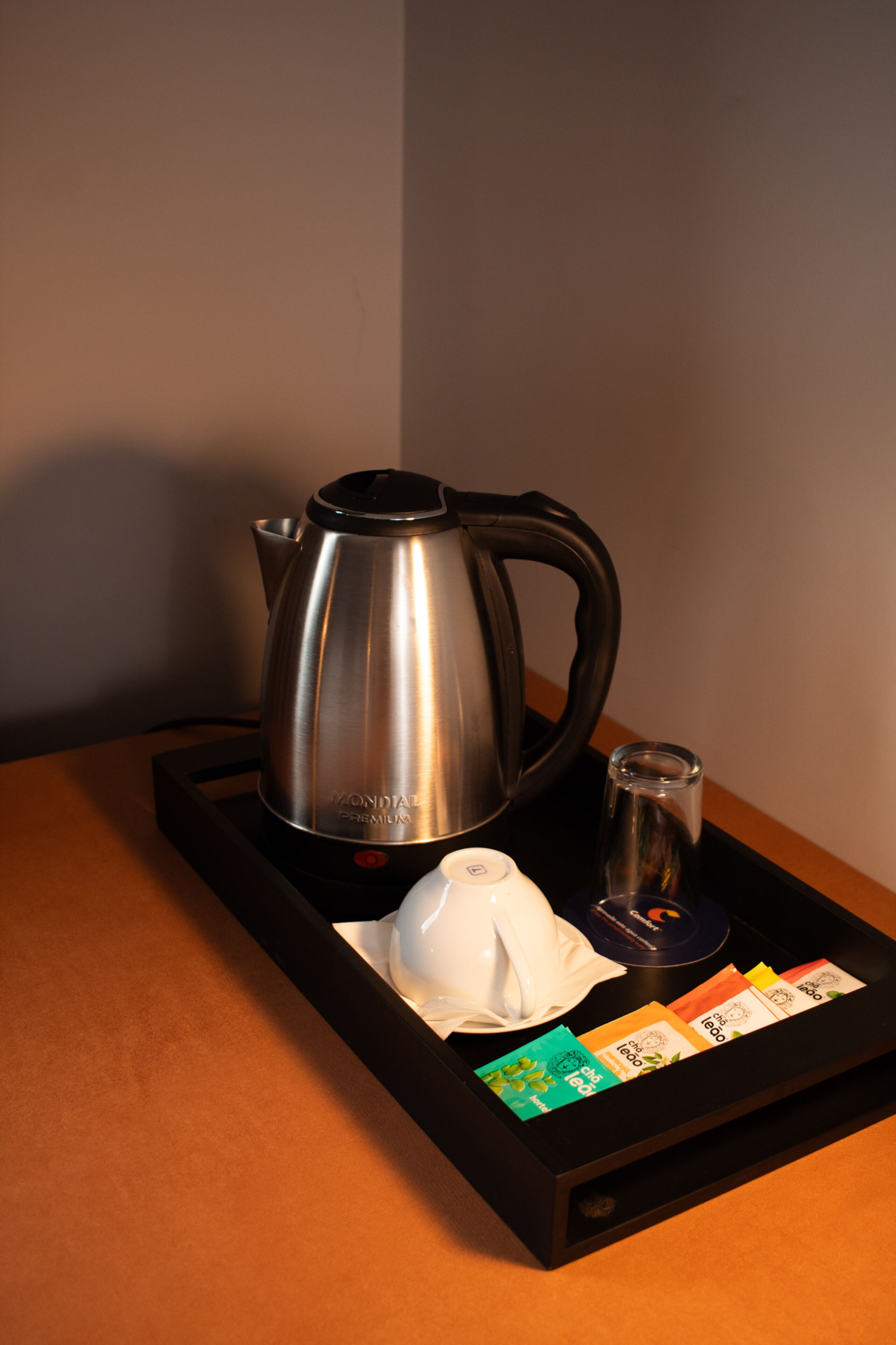 Una tetera de acero inoxidable, una tetera blanca, un vaso y bolsitas de té sobre una bandeja.